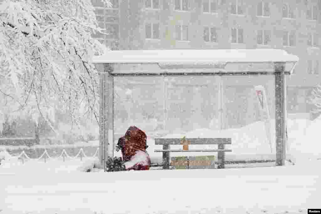 Una persona sin hogar sentada en una parada de autobús durante la tormenta de nieve.