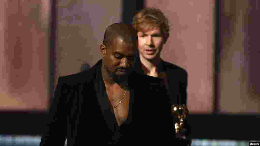 Beck, background, watches Kanye West, who pretended to take the stage after Beck won album of the year for "Morning Phase," at the 57th annual Grammy Awards in Los Angeles, California, Feb. 8, 2015.