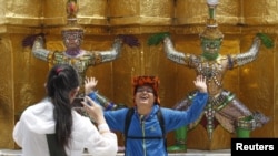 FILE - A Chinese tourist strikes a similar pose to statues as they visit the Grand Palace in Bangkok, March 23, 2015. 
