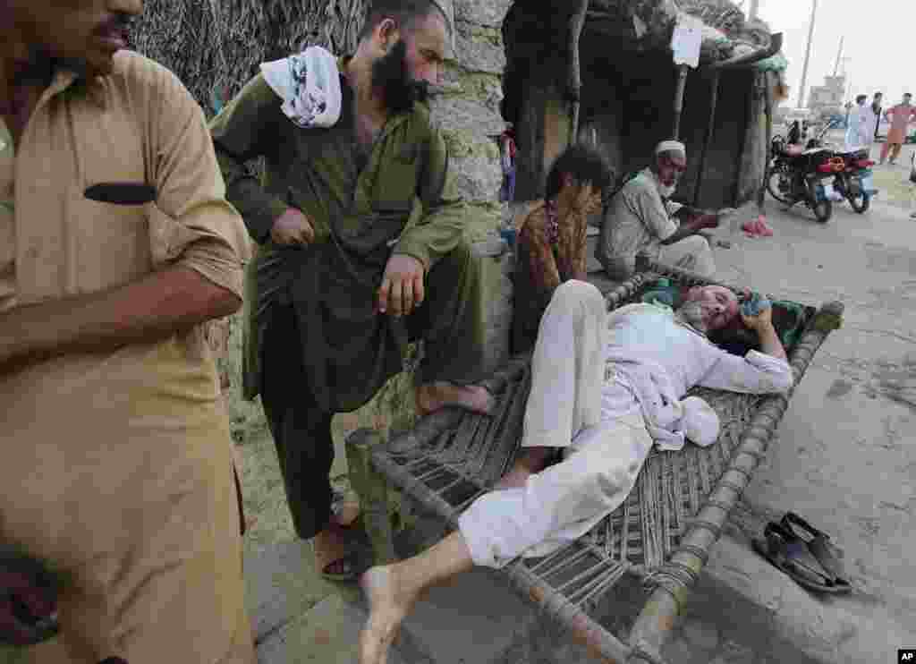 Afghan refugees wait for a transport to carry a sick man to a hospital while standing by him in a refugee camp situated in slums of Islamabad, Pakistan, June 19, 2014.