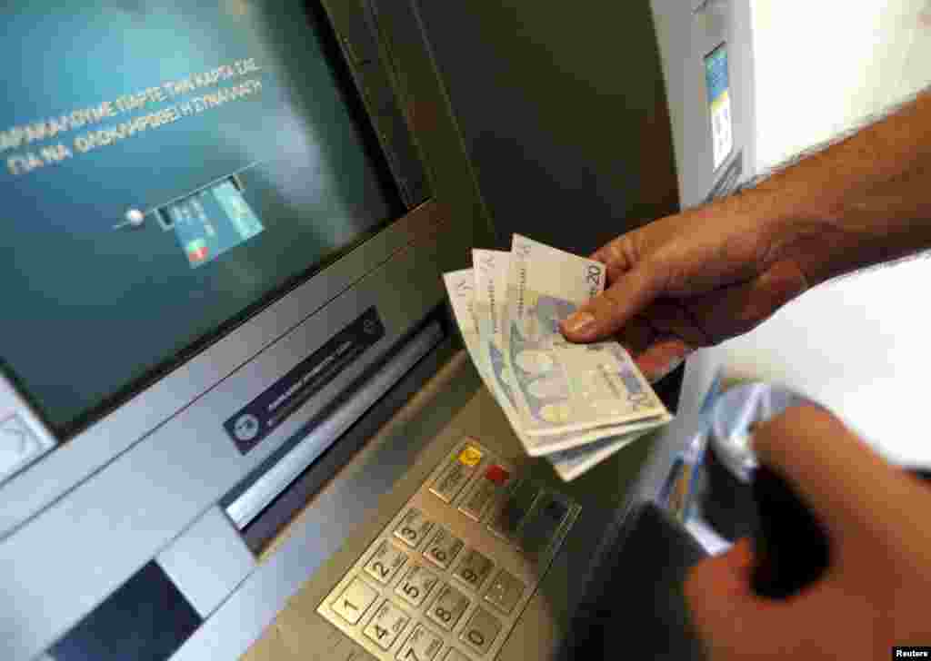 Seorang pria menarik uang 60 euro, batas maksimum yang diperbolehkan menyusul kontrol modal di bank-bank Yunani, di ATM National Bank of Greece di pelabuhan Piraeus dekat Athena (30/6). (Reuters/Yannis Behrakis)