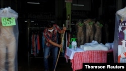 Un hombre limpia afuera del negocio de ropa donde trabaja en El Salvador, en la reapertura de la economía, en la fase uno. 6 de julio de 2020.