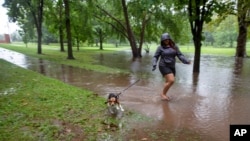 Una mujer pasea a su perro por un sendero inundado por la tormenta tropical Henri en Bushnell Park en Hartford, Connecticut, el domingo 22 de agosto de 2021 (AP Photo / Ted Shaffrey).