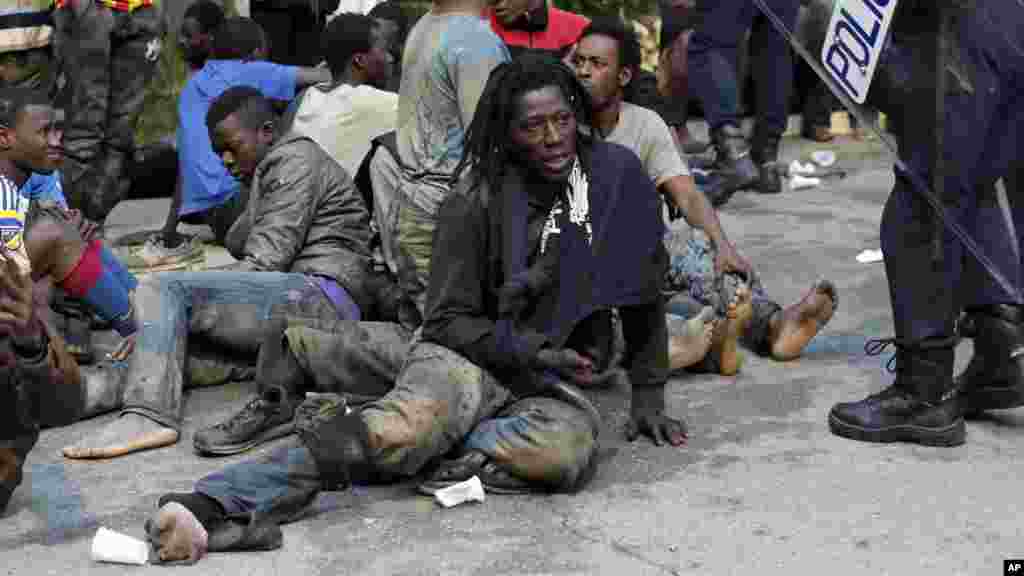 Les migrants sont assis sur le terrain près des policiers espagnols après avoir essayé d'entrer, dans l'enclave espagnole de Ceuta, le 17 février 2017.