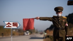 Seorang petugas keamanan publik menggunakan bendera merah untuk menghentikan taksi di jalan di pintu masuk Wonsan, Provinsi Kangwon, Korea Utara, sebagai bagian dari tindakan pencegahan terhadap virus COVID-19, 29 Oktober 2020. (Foto: dok).

