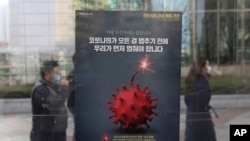 Orang-orang yang memakai masker melewati poster kampanye jarak sosial yang ditingkatkan di sebuah stasiun bus di Seoul, Korea Selatan, Senin, 7 Desember 2020. (Foto: AP)