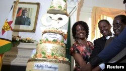 Presiden Zimbabwe Robert Mugabe (kanan) didampingi istrinya Grace (kiri) dan puteranya Chatunga (tengah) memotong kue ulang tahun ke-92 dalam perayaan di State House, Harare (22/2). 