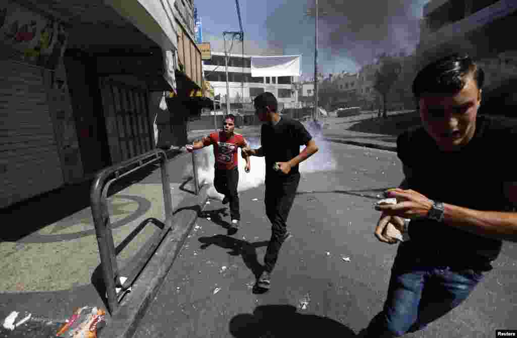 Protesters run from tear gas fired by Palestinian riot police in Hebron, Aug. 22, 2014.